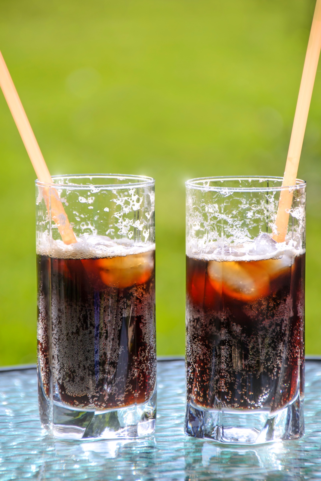 Two glasses of caramel beer with tubes and ice on a garden background - MEGA soft drinks
