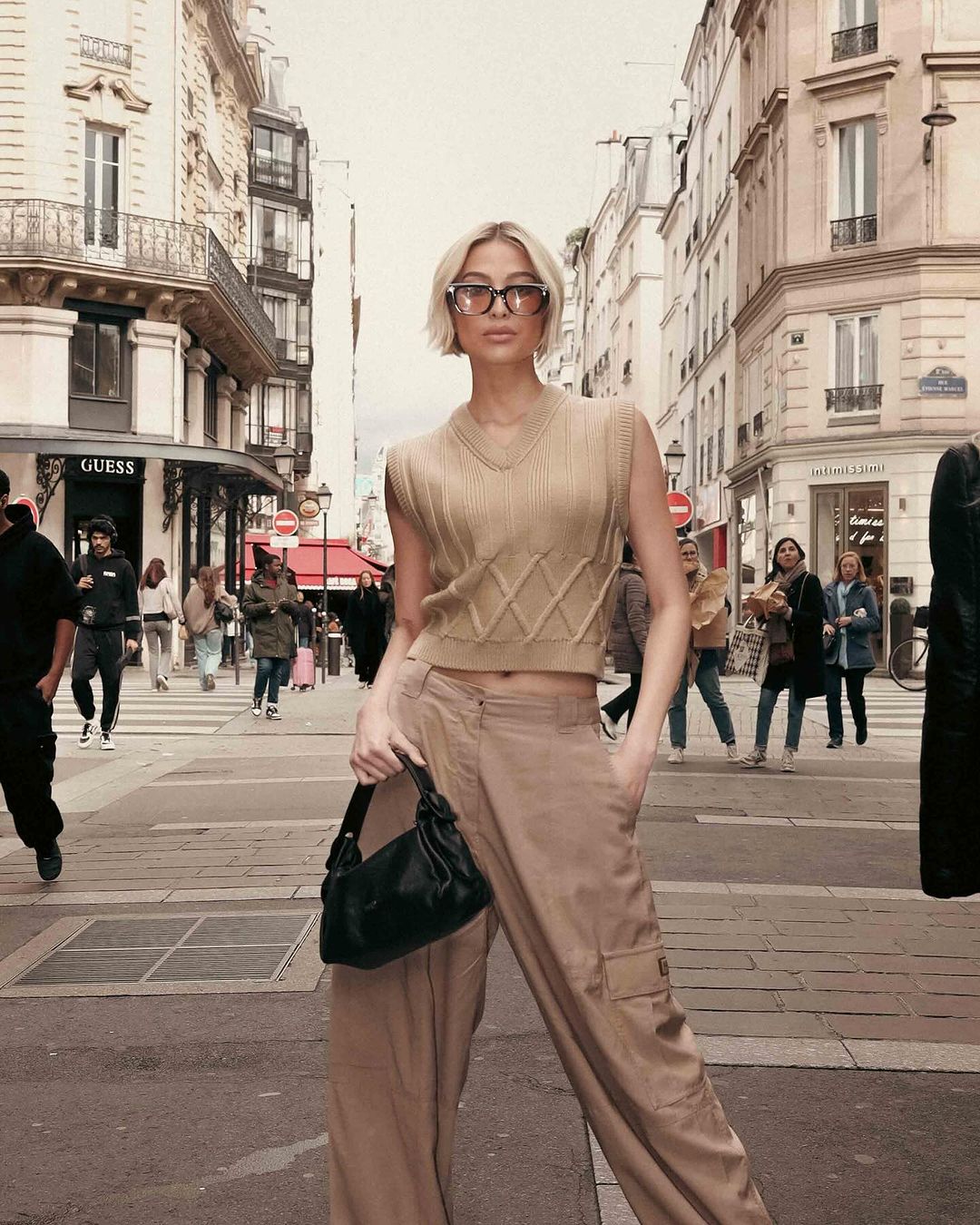 MMD - MEGA Michelle Dee wearing Kenzo: a knitted vest, cargo parachute pants, white boots, and a black leather bag during Paris Fashion Week